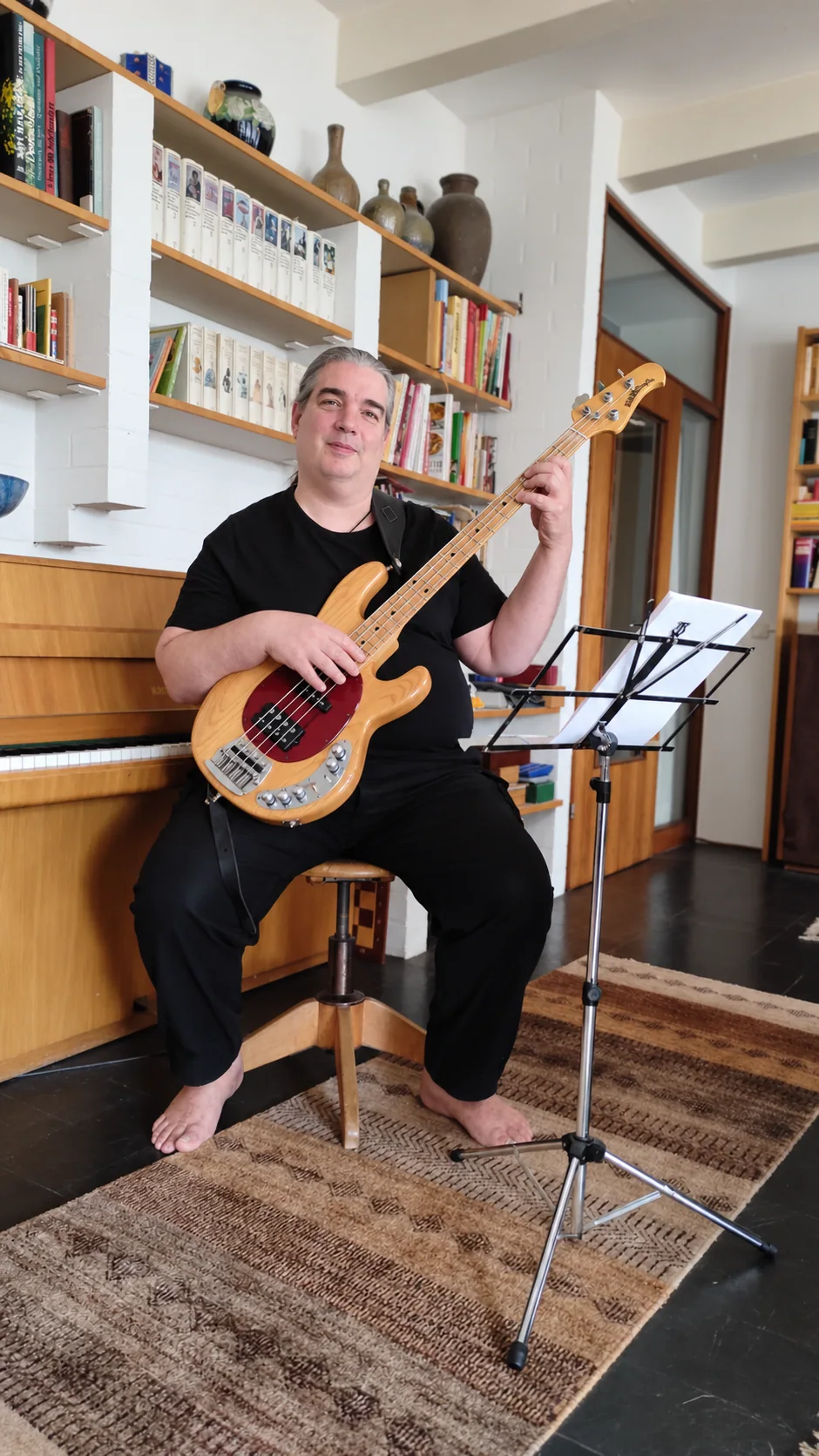 Sebastian Seifert mit seinem E-Bass vor Klavier und Bücherregal, daneben ein Notenständer